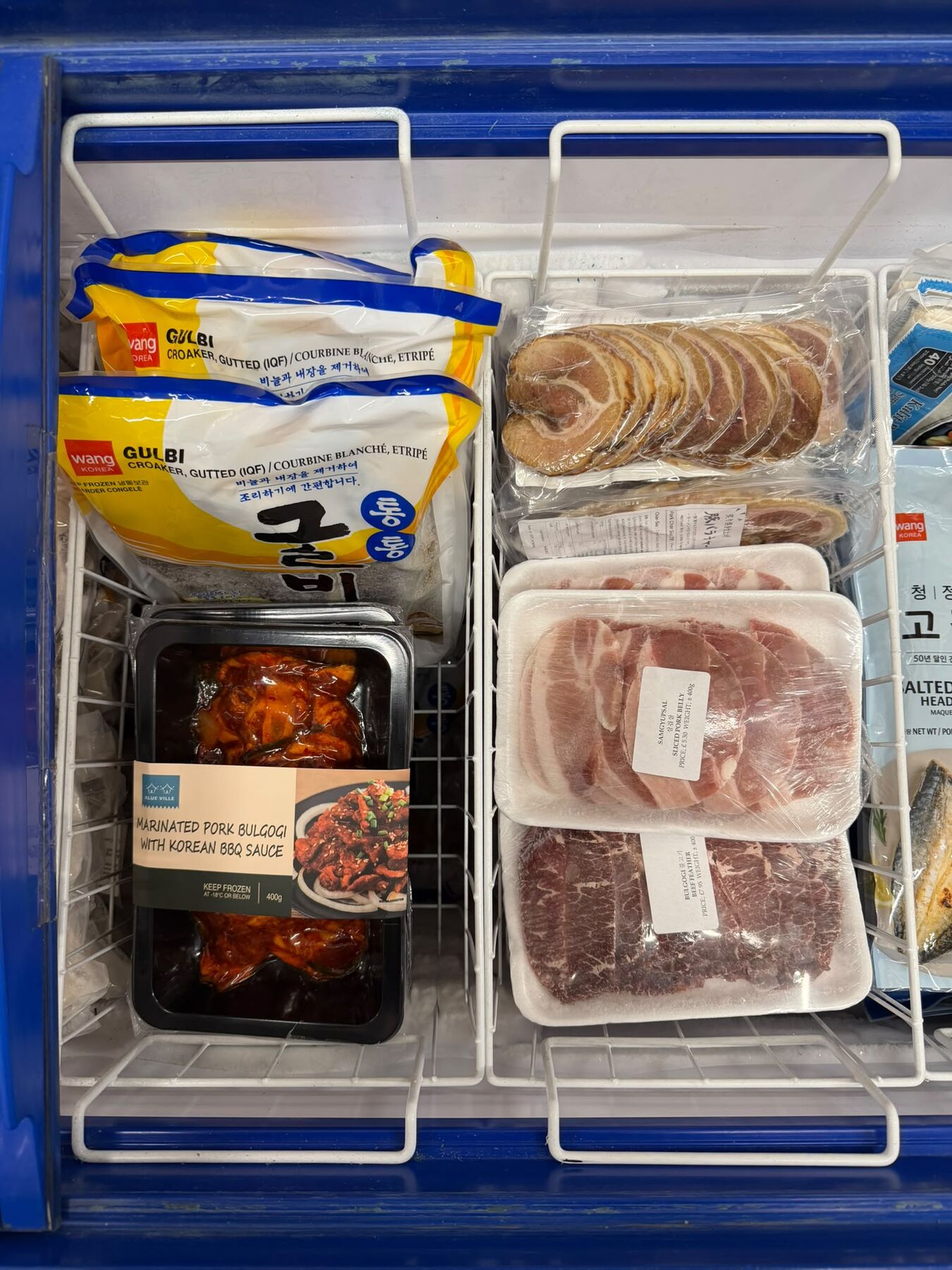 Freezer drawer of Korean BBQ meats and fish: marinated pork bulgogi in Korean BBQ sauce, sliced pork belly (samgyupsal), bulgogi beef, sliced char siu pork, frozen gulbi croaker and salted mackerel