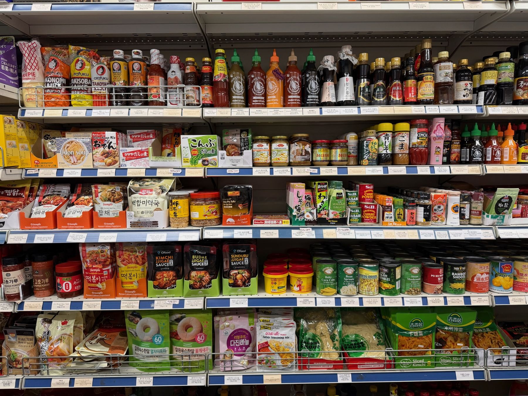 Shelves of sriracha, hoisin sauce, curry powder, wasabi, gochugaru, jjigae sauces, canned vegetables and kimchi